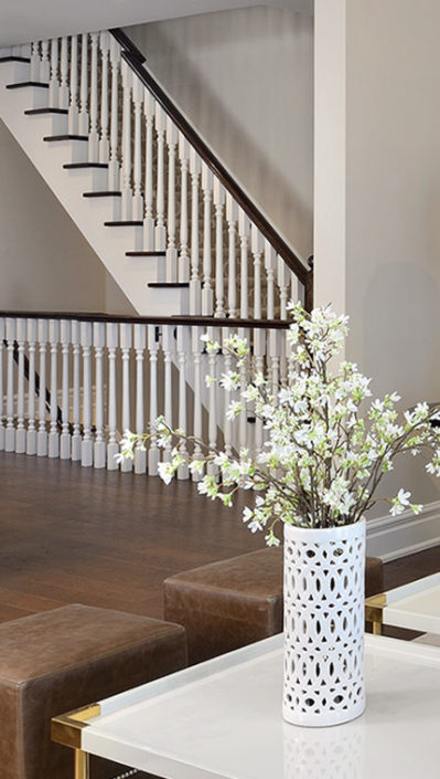 White flowers in a white vase with hardwood floors and a staircase in the background
